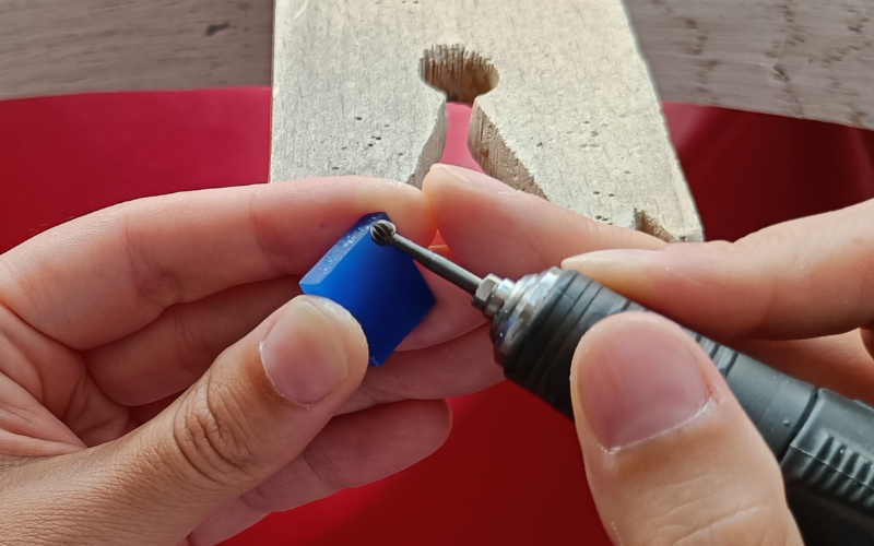 Close up of a hands holding a piece of wax and a burr. The way the wax is held, you burr on the top side 