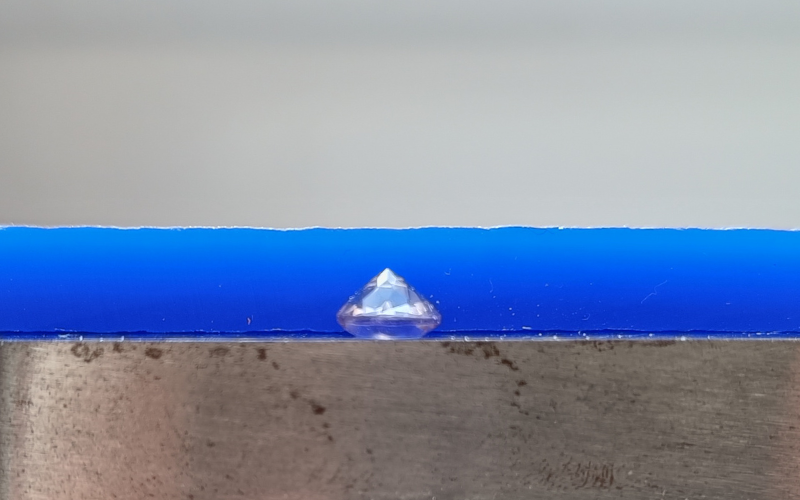 Close up of gemstone lying on top of a steel block with a piece of wax behind it that is much thicker than the gemstone