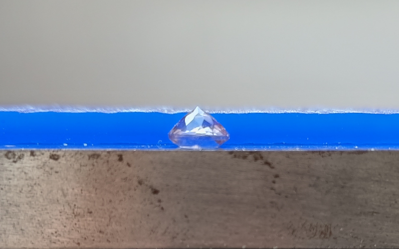 Close up of gemstone lying on top of a steel block with a piece of wax behind it that is thinner than the gemstone