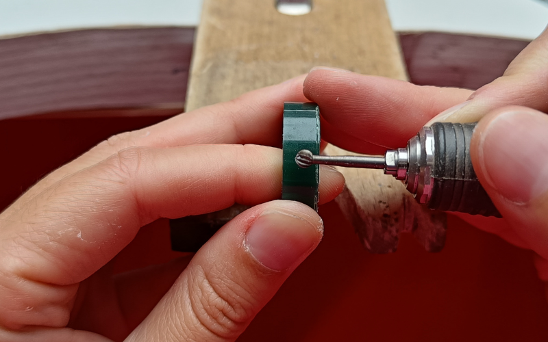 Close up of a hands holding a piece of ring wax and burr. The burr is in front of the ring wax and you can clearly see it 