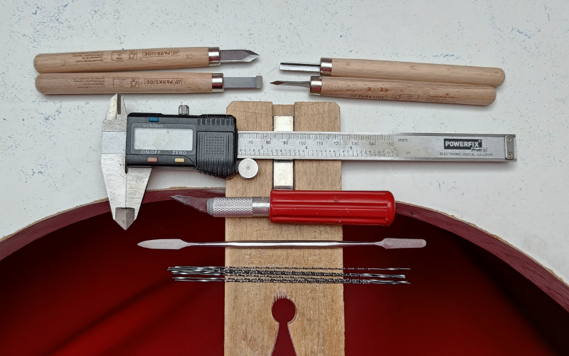 Bench with assortment of tools on top: 4 carving tools with wooden handle, callipers, stanley knife, dental cement spatula, spiral saw blades. 