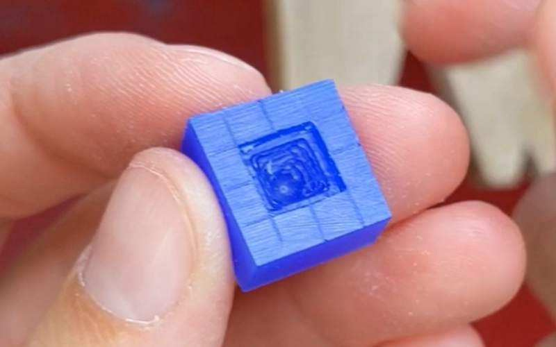 Close up of hands holding a piece of blue wax with a square opening removed. Lots of wax still on the walls sticking out