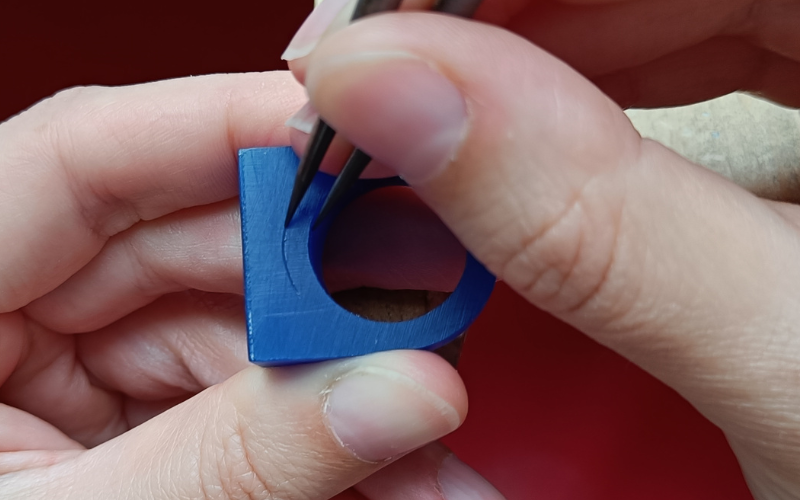 Close up of hands marking a line on a piece of blue ring tube using the ringsize as the guide