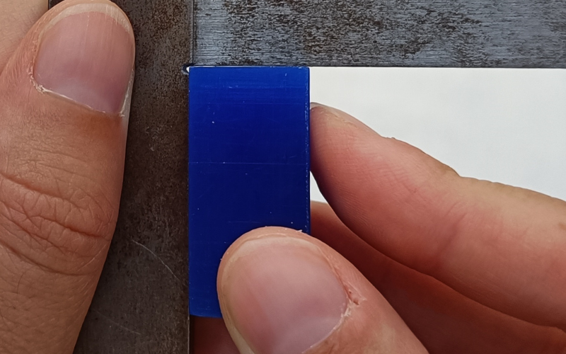 Close up of hands holding a set square and measuring a blue piece of wax in the corner. There is a gap visible on the top 