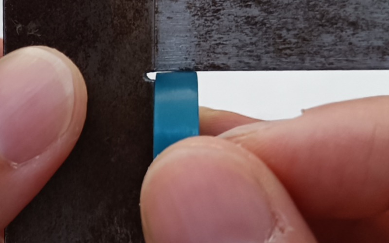Close up of hands holding a set square and measuring a turquoise ring. Gaps visible