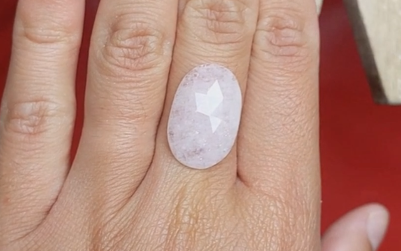 Close up of hands with a pink oval stone placed vertically over the middle finger.