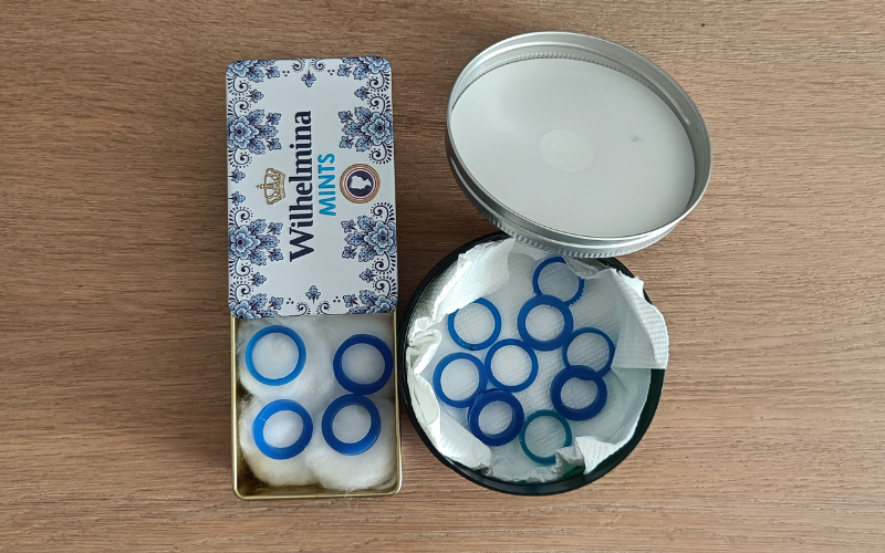 left a Wilhelmina mints tin lined with cotton wool with 4 blue wax rings on top, right a round plastic container lined with kitchen roll paper and a 9 blue wax rings laying on top 