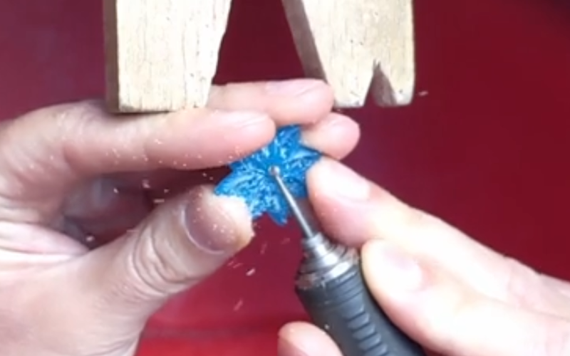 Close up of hands working at the bench.Teh left hand holds a piece of turquoise wax and the right hand is burring it