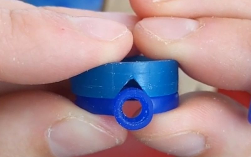 Close up of hands holding a finished solitaire ring from blue wax with the beginning of a turquoise wax wishbone ring on top.The triangle opening is cut out and trying the fit over the solitaire